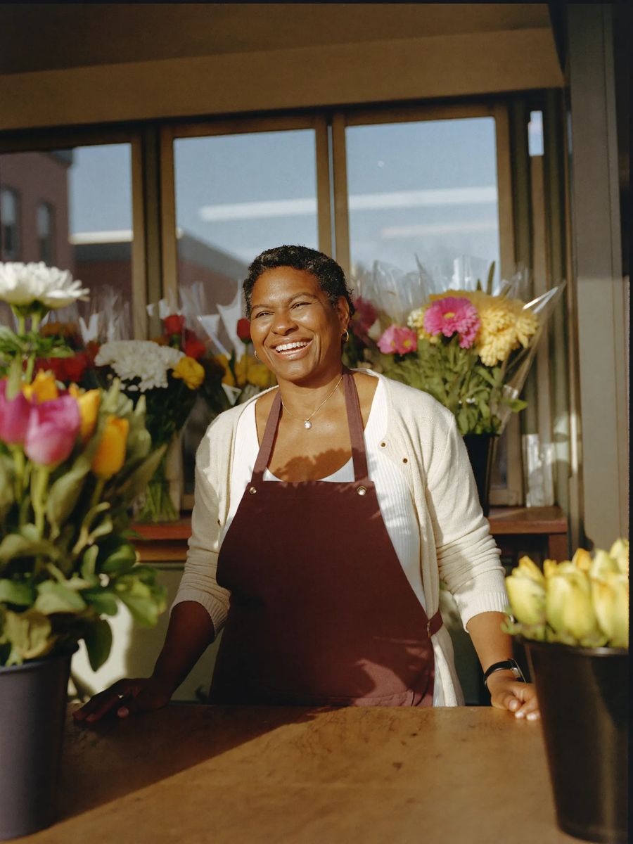 A smiling florist in her sixties behind the counter of her flower shop