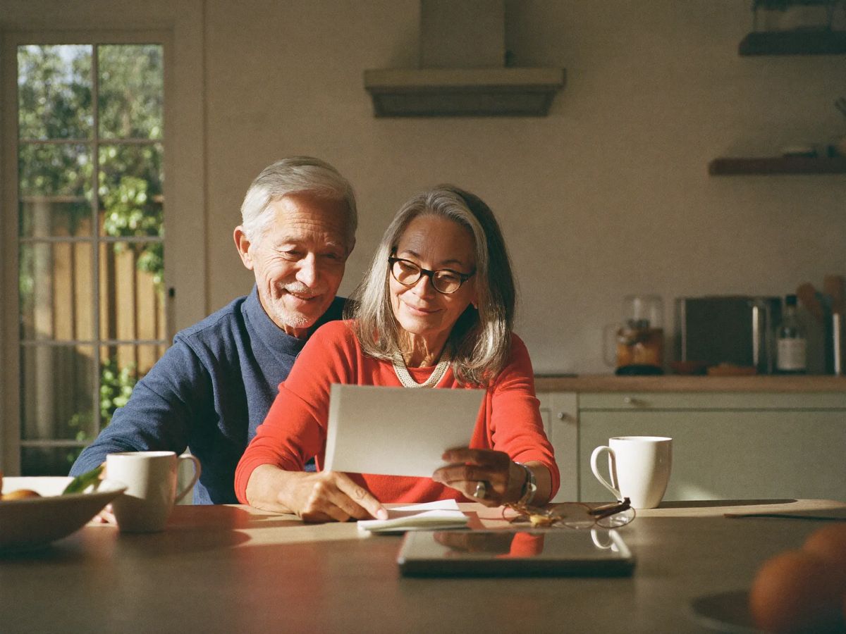 A couple in their sixties smiling at a page together at their kitchen table