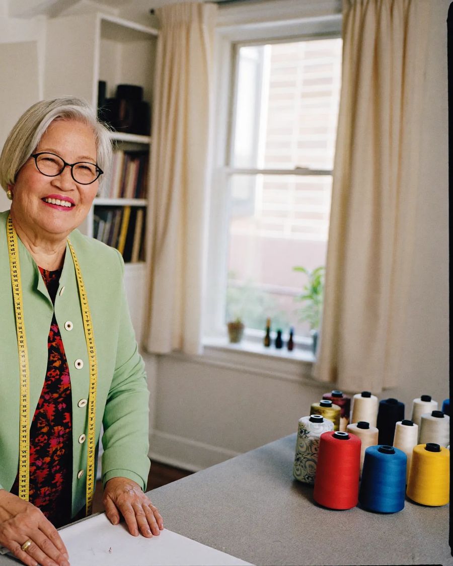 A tailor in her seventies smiling in her bright home studio